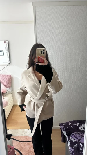 Beige omlottkappa med bälte - Stilren beige kappa med omlottknäppning och bälte i midjan. Jackan har klassisk krage, lång ärm och en clean look som passar perfekt till höst och vår. Materialet känns mjukt och har en lätt struktur. Snygg och enkel att matcha med allt.