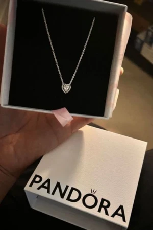 Pandora halsband med hjärthänge - Snyggt halsband från Pandora i silver med ett glittrigt hjärthänge. Kedjan är tunn och elegant, och hänget har små gnistrande stenar som ger extra bling. Perfekt för dig som gillar stilrena smycken med en romantisk touch.