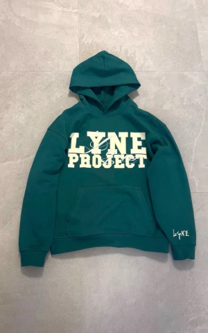 Grön hoodie från LYNE Project UF - Snygg mörkgrön hoodie från LYNE Project UF med stor vit print på bröstet och logga på ärmen. Tröjan har huva, känguruficka och är tillverkad i mjuk bomull. Perfekt för chill dagar och streetwear-stil. PRE ORDER BESTÄLL VIA DM PÅ INSTAGRAM 💚FINNS I STORLEK S-XL