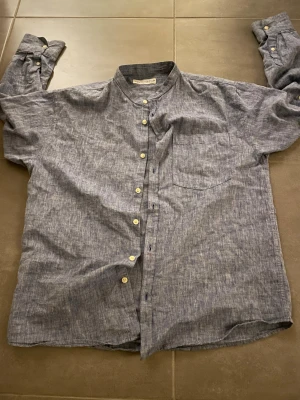 Blå linne zara-skjorta med knappar - Snygg blå skjorta från zara i linne med klassisk ståkrage och vita knappar hela vägen. Skjortan har en bröstficka och lång ärm, perfekt för en chill och stilren look.