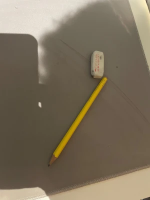 Penna och sudd. - Ingen bok syns på bilden, endast en gul blyertspenna och ett suddgummi på ett skrivbord. Ingen information om titel, författare eller innehåll kan utläsas från bilden.