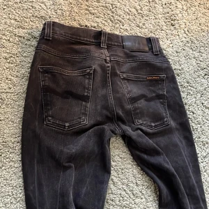 Svarta jeans från Nudie - Snygga svarta jeansbyxor från Nudie med klassisk femficksdesign. Jeansen har en snygg tvättlook. Byxorna har en normal passform och är tillverkade i ett slitstarkt material. Perfekta för en stilren look. Lite stretchiga. Wide: 28. Length: 30/31