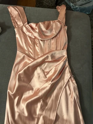 Champagnefärgad satin klänning Boohoo - Superfin kort klänning i champagnefärgad satin från Boohoo som endast testats, aldrig använt annars. Klänningen har breda axelband, draperad byst och markerad midja med snygga sömmar. Materialet är glansigt och känns lyxigt, perfekt för dig som vill sticka ut. Stängs med dragkedja i sidan.