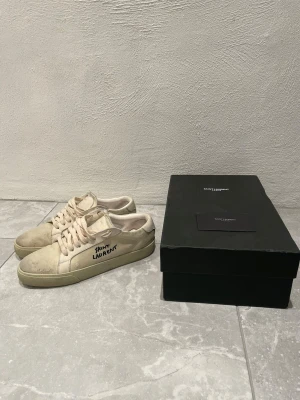 Saint Laurent beige sneakers - Snygga beige sneakers från Saint Laurent med handskriven logga på sidan. Skorna har rund tå, platt sula och snörning. Materialet är en mix av mocka och skinn, vilket ger en lyxig känsla. Perfekt för dig som gillar stilrena och exklusiva sneakers. Storlek 40 men passar även dig som har storlek 41.