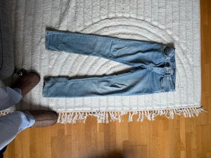 Nudie Jeans Grimtim (Slim) passar ca 183-188 - Säljer ett par ljusblå jeans från Nudie Jeans med klassisk femficksdesign och snygga kontrastsömmar. Jeansen har raka ben och är tillverkade i mjukt bomullsdenim. Bakfickorna har Nudie Jeans ikoniska broderade vågmönster.
