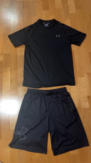 Under armour träningsset - Snyggt träningsset ifrån under armour, T-shirt och shorts. Kläderna är i ett skönt material perfekt inför all slags träning. Dom är i storlek S men kan passa M också. Dom är i bra skick så jag bara använt dom 2 gånger. Pris kan diskuteras vid snabb affär.