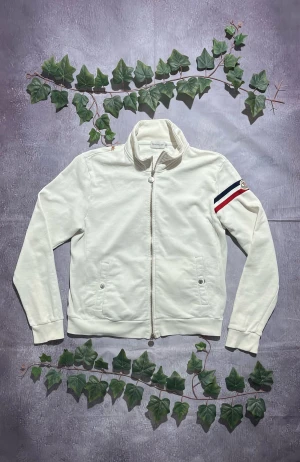Moncler vit Sweatshirt storlek M [ÄKTA] - 🎨 Färg: Vit 📏 Storlek: Medium (M) ♻️ Skick: 8/10 – mindre bruksspår, men inga större defekter 🧵 Material: Bomullsblandat sweatshirt-tyg ✨ Detaljer: • Mjuk och bekväm tröjjacka • Hög krage • Två fickor med knappdetaljer • Tvåvägsdragkedja • Moncler-logga på vänster ärm • Röd, vit och marinblå randdetalj på ärmen • Ribbstickade muddar och nederkant • Stilren och lättburen – perfekt till vardags ‼️ Skickas dagen efter köpet genomförs! ‼️