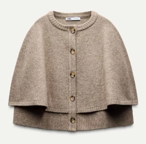 Beige kofta med knappar från Zara - Säljer en beige kofta från Zara med rund hals och ribbade kanter. Koftan har en unik cape-liknande form och är försedd med fem snygga knappar framtill. Materialet är mjukt och stickat, perfekt för lager-på-lager under kyliga dagar.