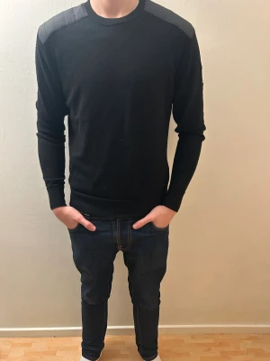 Svart långärmad tröja från Belstaff - Svart långärmad tröja från Belstaff med coola quiltade detaljer på axlarna. Ärmarna är gjorda av merinoull. Kvitto och prislapp ingår. Nypris: 2500 kr 