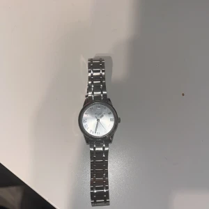 Silverfärgad klocka från Regal - Stilren klocka från Regal med rund urtavla i silver och romerska siffror. Länken är i blankt metallmaterial och har ett klassiskt, tidlöst utseende. Perfekt accessoar för dig som gillar minimalistisk design och metallarmband.Pris kan diskuteras…