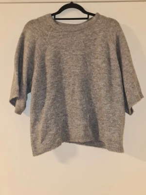 Grå stickad tröja med kort ärm - Mysig grå stickad tröja med rund halsringning och korta ärmar. Tröjan har en avslappnad passform och är perfekt för lager-på-lager under höst och vinter. Enkel och stilren design som passar till det mesta.