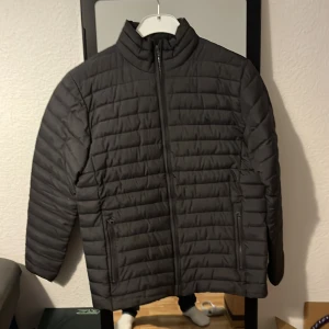 Svart pufferjacka från Joules - Säljer en svart pufferjacka från Joules i storlek small. Jackan har horisontella quiltade paneler, hög krage och dragkedja framtill. Två sidofickor med dragkedja och stilren look som funkar till de flesta outfits. Materialet är polyester.