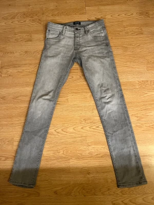 Jack & Jones slim/glenn  - Snygga grå jeans från Jack & Jones i slim fit modell. Klassisk femficksdesign med svarta detaljer på bakfickorna och svart jack & Jones -lapp i midjan. Jeansen har raka ben och är tillverkade i mjukt jeanstyg med lite stretch för skön passform. Strl 29/34