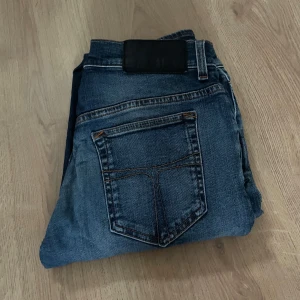 Blå jeans med klassisk passform - Snygga blå jeans med klassisk femficksdesign och kontrastsömmar. Jeansen har en mörkblå tvätt med lätt slitning och en svart patch bak i midjan. Perfekta för dig som gillar en tidlös look och vill ha ett par jeans som funkar till det mesta. Väldigt snygga jeans. Storlek 28/32. Hör av dig vid fundering! Kan gå ner i pris vid snabbt köp!