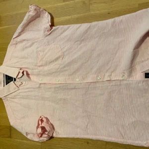 Randig rosa kortärmad skjorta Bondelid - Fräsch kortärmad skjorta från Bondelid i ljusrosa och vit randigt mönster. Skjortan har klassisk krage, bröstficka och knappar framtill. Tillverkad i mjuk bomull som känns lätt och skön mot huden. Perfekt för varma dagar och en chill stil.