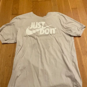 Nike Just Do It t-shirt i vitt - Nike t-shirt i vitt med den klassiska 'Just Do It' loggan tryckt i vitt på bröstet. Modellen har rund hals och korta ärmar, tillverkad i mjuk bomull som är skön mot huden. Perfekt för dig som gillar sportiga och stilrena plagg.