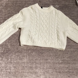 Vit stickad croppad tröja H&M XXS - Superfin vit stickad tröja från H&M i croppad modell. Tröjan har flätstickat mönster framtill, ribbad halsringning och långa ärmar. Perfekt för lager-på-lager och passar till både jeans och kjol.