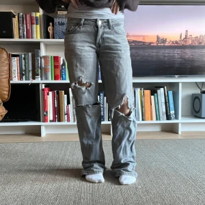 Grå slitna baggy jeans - Grå baggy jeans med slitningar. Klassisk femficksmodell med låg midja och avslappnad passform. Perfekta för en avslappnad och edgy stil.