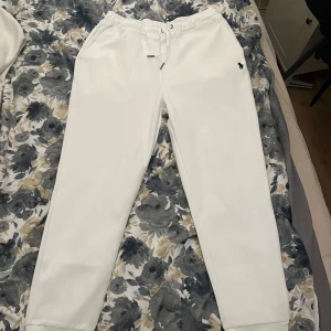 Vita mjukisbyxor från Ralph Lauren - Snygga vita mjukisbyxor från Ralph Lauren med klassisk logga broderad på höften. Byxorna har dragsko i midjan och ribbade muddar vid bensluten. Perfekta för en chill och avslappnad stil.