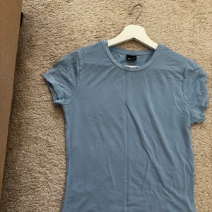 Blå basic t-shirt från Gina Tricot - En stilren blå t-shirt från Gina Tricot i mjuk bomull. Modellen är klassisk med rund halsringning och korta ärmar. Perfekt att matcha med jeans eller kjol för en enkel och snygg look. Ej använd