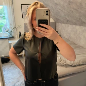 Svart skinnimitation topp Gina Tricot - Cool svart topp i skinnimitation från Gina Tricot. Modellen är croppad med korta ärmar och rund halsringning. Perfekt att styla med jeans eller kjol för en trendig look.