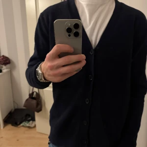 Mörkblå kofta från Kappahl, storlek S - Säljer en stilren mörkblå kofta från Kappahl i storlek S. Koftan har v-ringning, knäppning framtill med fem knappar och långa ärmar. Perfekt att slänga över en t-shirt eller skjorta för en clean look. Materialet är mjukt och känns skönt mot huden.