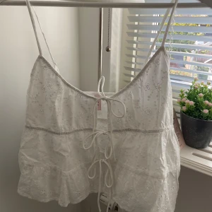 Vit broderad linnetopp från Nelly - Superfin vit linnetopp från Nelly med tunna axelband och broderade blommor. Toppen har snörning i ryggen och volangdetaljer nertill. Perfekt för sommarens alla tillfällen och ger en romantisk vibe.
