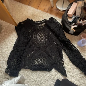 Svart spetsblus med lång ärm - Säljer en svart blus i spets med lång ärm och vackra cirkulära broderade detaljer. Blusen är genombruten och har en elegant, bohemisk känsla. Perfekt att styla med jeans eller kjol för en cool look.
