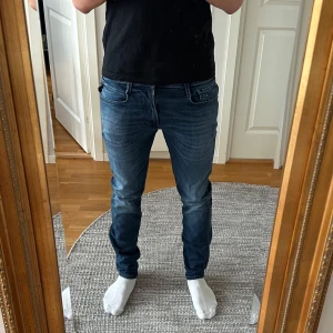 Replay Anbass jeans i mörkblå denim - Snygga Replay Anbass jeans i mörkblå tvätt med diskreta slitningar och klassiska fem fickor. Jeansen har smal passform och raka ben, med detaljerad söm på bakfickorna och svart Replay-lapp i midjan.