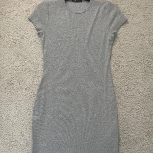 Grå kortärmad klänning - En enkel och stilren grå klänning med tight passform. har rund halsringning och korta ärmar. Perfekt för dig som gillar minimalistisk stil och vill ha något bekvämt men ändå snyggt.