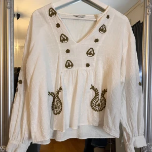 Vit blus med grön brodering - Jättefin vit blus med grön brodering. Väldigt luftig och super fin till allt! Den har fin V ringning och även knappar på ärmarna så man kan välja ha stängda ärmar eller mer öppet. Väldigt bra skick!💕