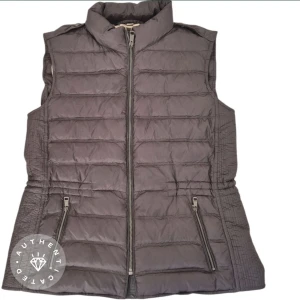 mörkgrå  och brun rutig dunväst Burberry women L - Snygg dunväst från Burberry med klassiskt rutigt mönster i mörkgrå, brunt, svart och rött. Västen har hög krage, dragkedja framtill och två fickor med dragkedja. Perfekt för lager-på-lager och ger en cool vibe till din outfit.