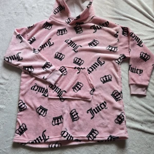 Juicy Couture rosa fleecehoodie - Supermjuk rosa hoodie från Juicy Couture i fleece med svart kronmönster och logga över hela tröjan. Har huva, lång ärm och stor magficka. Perfekt för dig som älskar cozy vibes och statement-plagg.