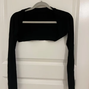 Svart croppad kofta - Svart croppad kofta med lång ärm, tillverkad i 100% viskos. Enkel och stilren design som passar perfekt över ett linne eller klänning. Snygg att slänga på sig för en extra touch till outfiten. Storlek S och XS. 