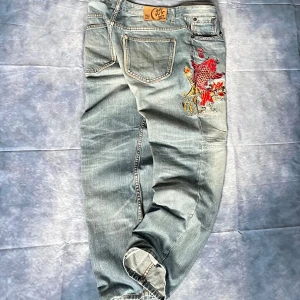 Nippon Blue Y2K Embroidered Koi Fish Jeans - 🔥 Rare Nippon Blue Japanese denim jeans featuring detailed red koi fish embroidery on the back pocket and front leg. Light wash denim with natural fading and distressed details for an authentic vintage look. Wide/straight leg cut – perfect for Y2K and streetwear fits.  W36/L32  Waist: 44 Hips:49,5 Back rise: 37 Thigh: 33 Knee: 24 Leg opening 21 Inseam 75,5 Outseam 103  ✨ Unique Japanese-inspired embroidery makes these jeans a statement piece.  Condition: Pre-loved, some repairs and natural wear/
