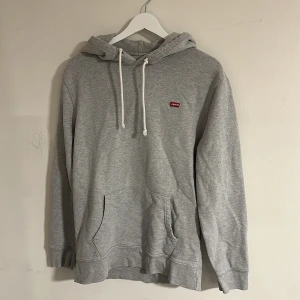 Grå hoodie från Levi's - Säljer en stilren grå hoodie från Levi's i storlek S. Tröjan har klassisk huva med vita snören, magficka och liten röd Levi's-logga på bröstet. Perfekt för chill dagar och enkel att matcha med jeans eller joggers. Storleken är S men funkar även till M. En liten färgfläck som inte är särskilt märkvärd men därav priset (se bild 5). Skriv vid minsta fundering🍾🌠