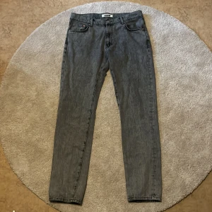 Grå jeans från Woodbird, straight fit - Säljer ett par grå jeans från Woodbird i rak modell. Jeansen har klassisk femficksdesign, bälteshällor och läderpatch med logga bak. Materialet är denim i bomull och färgen är tvättad grå som ger en cool vintagekänsla.