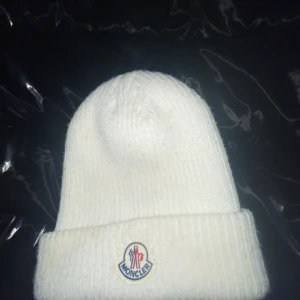 Vit ribbad mössa från Moncler - Snygg vit mössa från Moncler med ribbad struktur och uppvikt kant. Märkets klassiska logga sitter framtill och insidan har en Moncler-etikett. Perfekt för dig som vill ha en clean och stilren look under kalla dagar. Är [ÄKTA] 