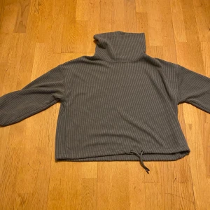 Grå ribbad polotröja från F&F - Mysig grå polotröja från F&F i ribbat material. Tröjan har hög krage, långa ärmar och en dragsko nertill för en snygg passform. Perfekt för lager-på-lager och chill dagar.