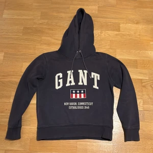 Mörkblå hoodie från GANT med tryck - Tjena folket! Nu säljer jag min sköna GANT hoodie! Den är blå med fin logga och GANT text! Fina detaljer och klassiska hoodiesnören vid luvan! Skriv vid minsta fråga! 
