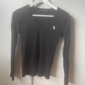 Svart långärmad tröja Polo Ralph Lauren - Svart långärmad tröja från Polo Ralph Lauren med v-ringning och klassisk vit logga broderad på bröstet. Stilren och passar till allt!🤩