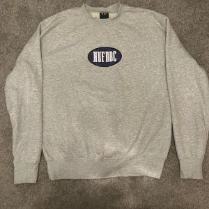 Grå sweatshirt från HUF med tryck - Grå sweatshirt från HUF i storlek L med stort lila och vitt HUF DBC-tryck på bröstet. 