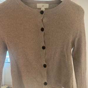 Beige ribbad kofta från H&M  - Snygg beige ribbad kofta från H&M i storlek XS. Långa ärmar och svarta knappar framtill. Mjuk och skön. 