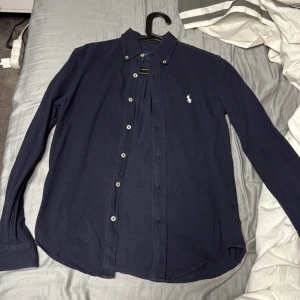 Mörkblå skjorta från Ralph Lauren XS - Snygg mörkblå skjorta från Ralph Lauren i lätt och luftig bomull. Klassisk button-down krage, vita knappar och ikonisk broderad logga på bröstet. Perfekt för dig som gillar stilrena och tidlösa plagg med premiumkänsla.