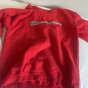 Röd Champion sweatshirt med broderad logga - Röd sweatshirt från Champion med broderad logga över bröstet. Klassisk modell med rund hals och långa ärmar. Mjuk insida i fleece som gör den extra skön. Perfekt för dig som gillar sportig och avslappnad stil.