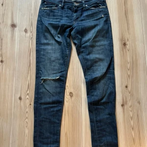 Ralph Lauren Denim & Supply skinny jeans - Mörkblå skinny jeans från Ralph Lauren Denim & Supply med slitningar och trasig detalj på ena benet. Klassisk femficksmodell med dragkedjegylf och snygga kontrastsömmar. Perfekta för en avslappnad och cool look.