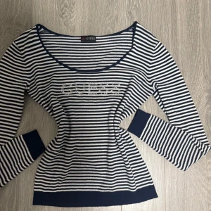 Randig långärmad tröja från Guess - Snygg långärmad tröja från Guess med marinblå och vita ränder. Tröjan har rund halsringning och Guess-loggan framtill i glittriga stenar. Muddar vid ärmslut och nederkant ger en schysst passform. Perfekt för dig som gillar klassisk men trendig stil.