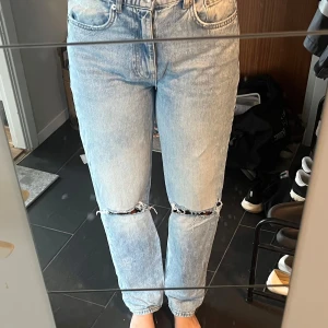Ljusblå ripped jeans med raka ben - Säljer ett par ljusblå jeans med slitna hål över knäna och klassisk femficksdesign. Jeansen har raka ben och en avslappnad passform, perfekt för en chill och trendig look. Materialet är klassisk denim i bomull.