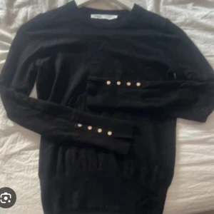 Svart långärmad tröja med guldknappar - Svart långärmad tröja från Zara med snygga guldknappar längs ärmsluten. Tröjan har en klassisk rund halsringning och är i mjukt material som sitter skönt på kroppen. Perfekt för dig som gillar stilrena detaljer. Lånad bild, skrev för bilder och pris kan diskuteras!🥰