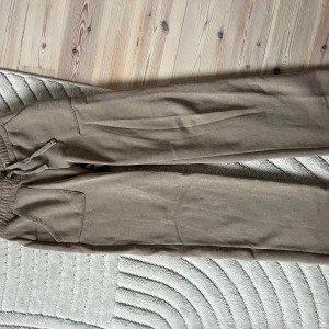 Beige mjukisbyxor med fickor - Säljer ett par beige mjukisbyxor med elastisk midja och dragsko. Byxorna har en enkel design med synliga sömmar och praktiska fickor framtill. 